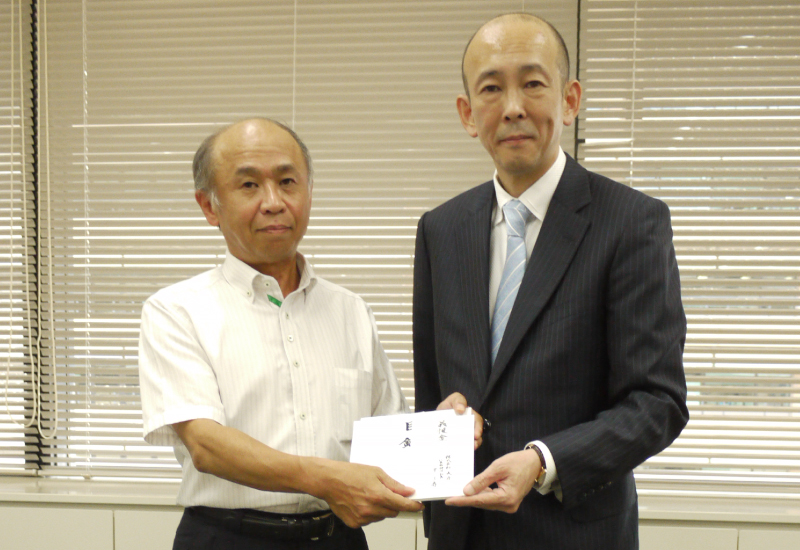 熊本県教育庁教育理事　金子　徳政様（左）に、当社　代表 取締役社長　平　了寿から義援金の目録および小切手をお渡し しました（2016年8月26日）